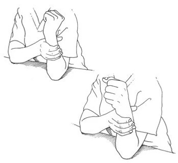 Man sitting at a table with one elbow on a table. The arm placed arm-wrestling position. The other hand grips around the forearm..
