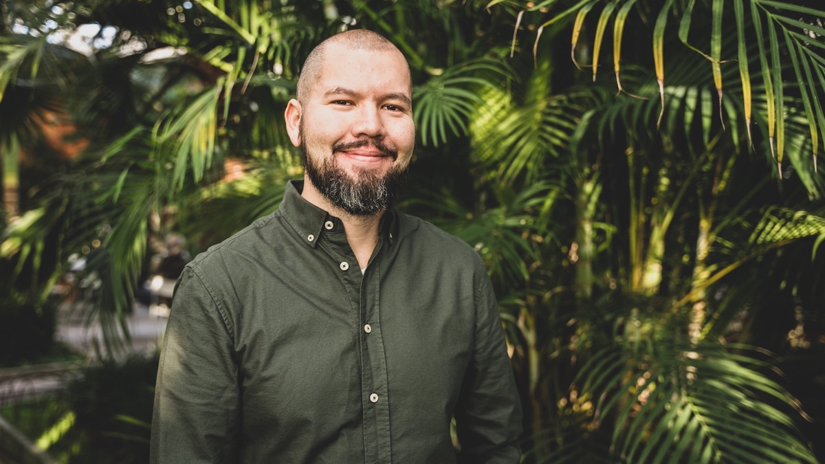 En man med skägg står framför palmer.