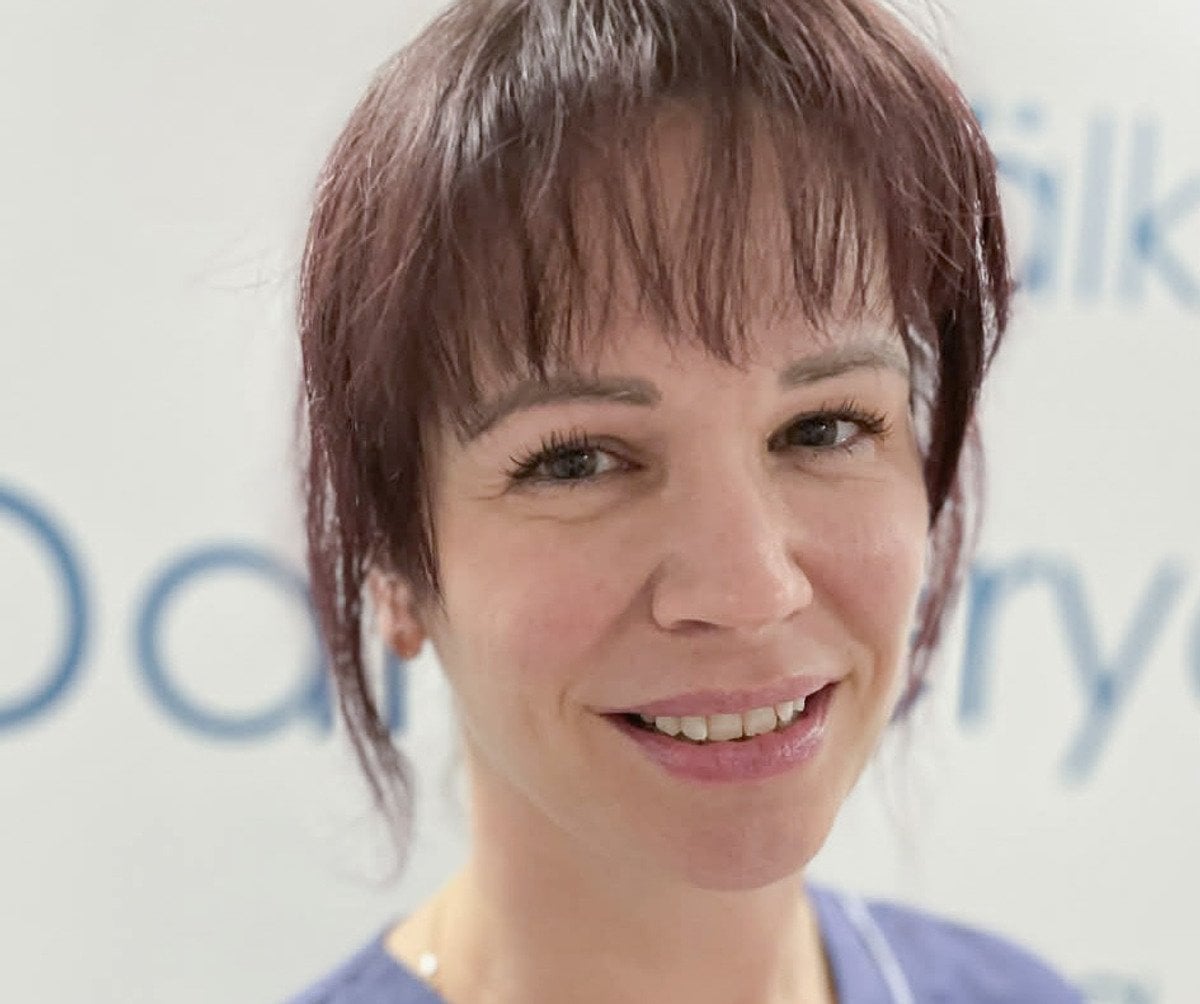 En kvinna i operationskläder ler mot kameran.