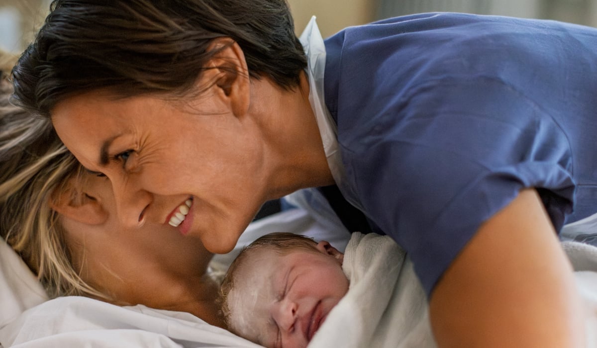 Barnmorska står lutad över en kvinna och hennes nyfödda bebis.