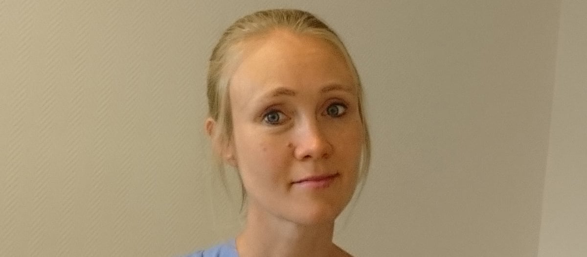 En kvinna i operationskläder håller i en flaska med medicin.