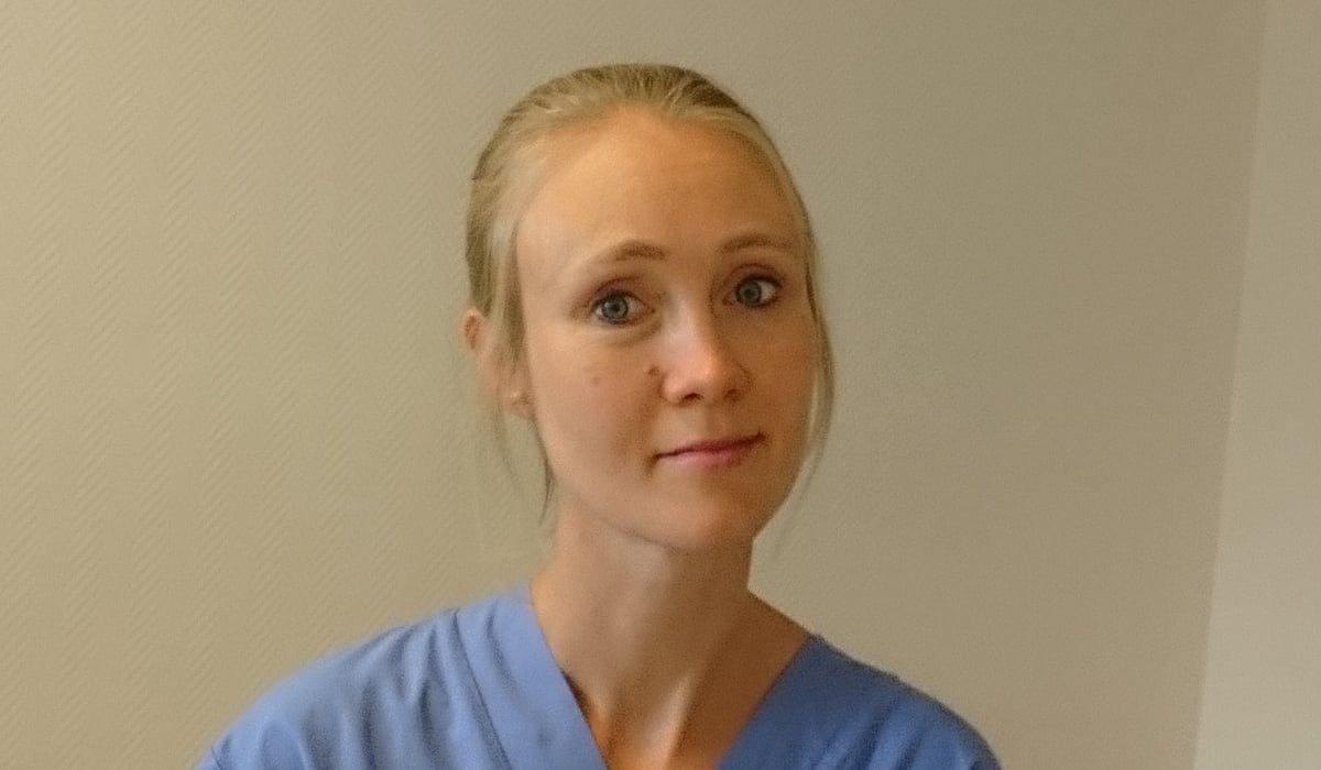 En kvinna i operationskläder håller i en flaska med medicin.