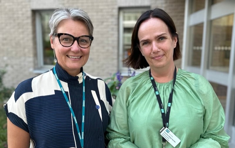 Två kvinnor står bredvid varandra framför en byggnad.