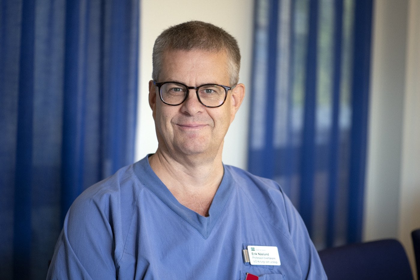 En man i blå skrubbdräkt och glasögon.